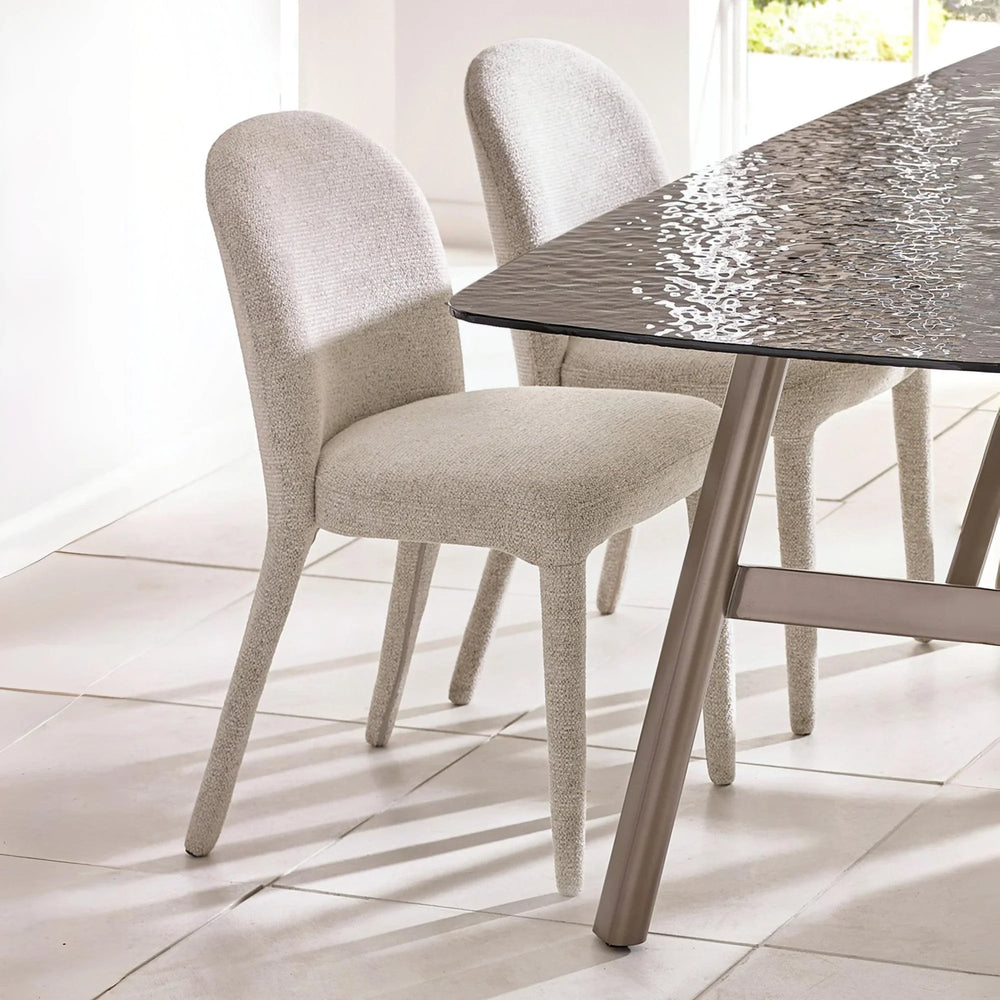 Beige fabric dining chairs with curved backs beside a modern glass dining table