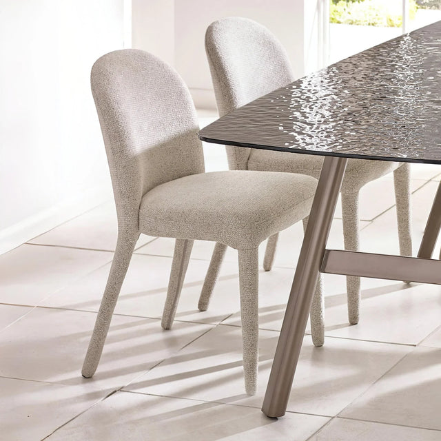 Beige fabric dining chairs with curved backs beside a modern glass dining table