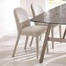 Beige fabric dining chairs with curved backs beside a modern glass dining table