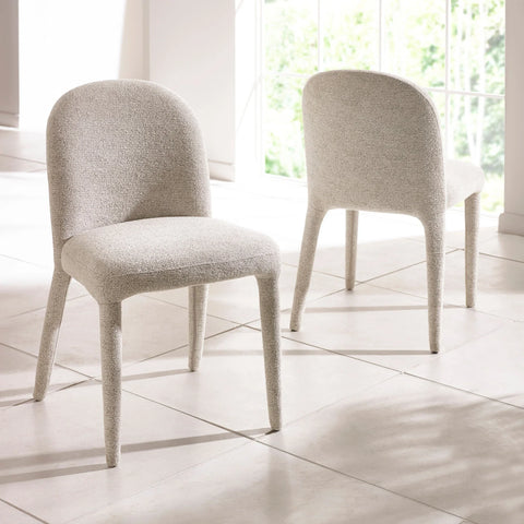 Pair of cream boucle dining chairs with curved backs on tiled floor near window