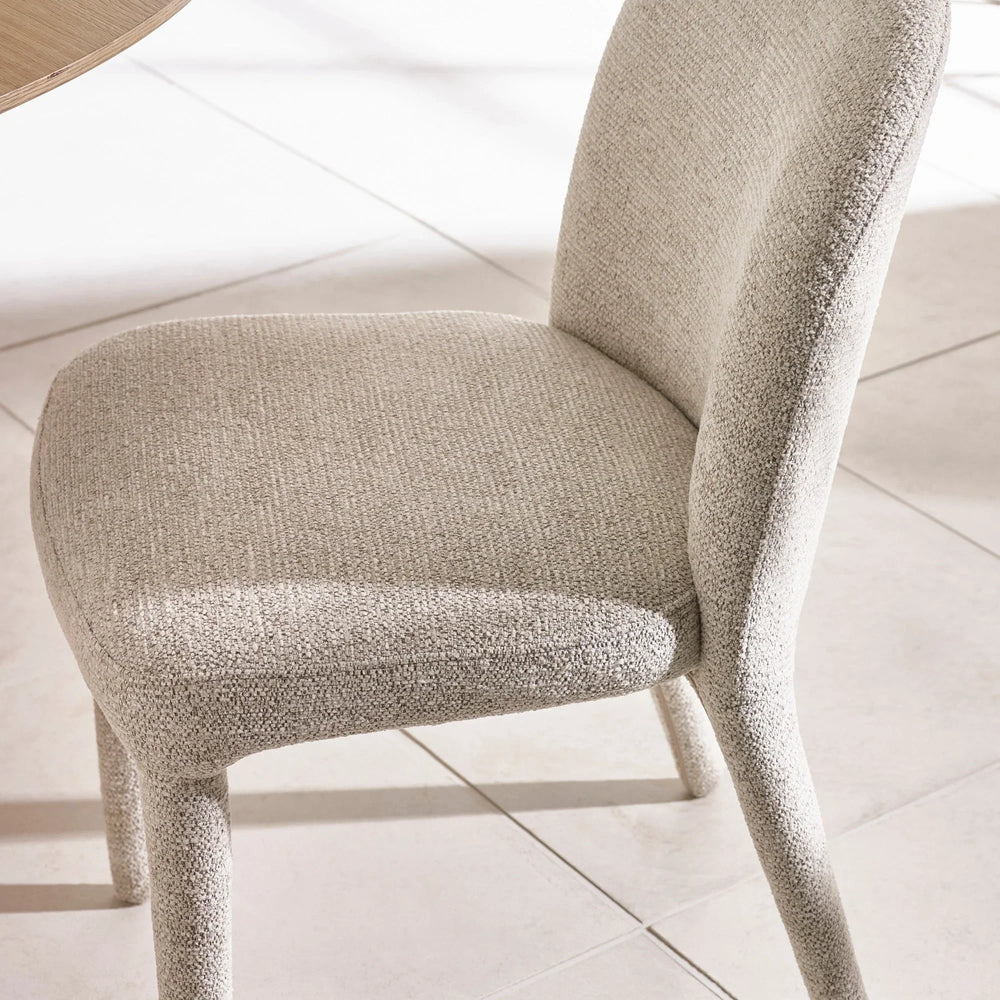 Light beige upholstered dining chair with curved back on tiled floor
