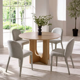 Round oak dining table with four grey upholstered chairs in a bright modern dining room