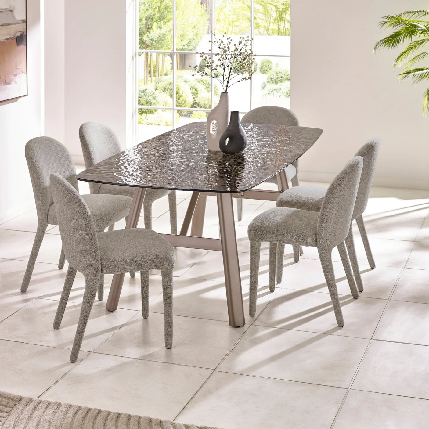 Glass dining table with six grey upholstered chairs in modern bright dining room