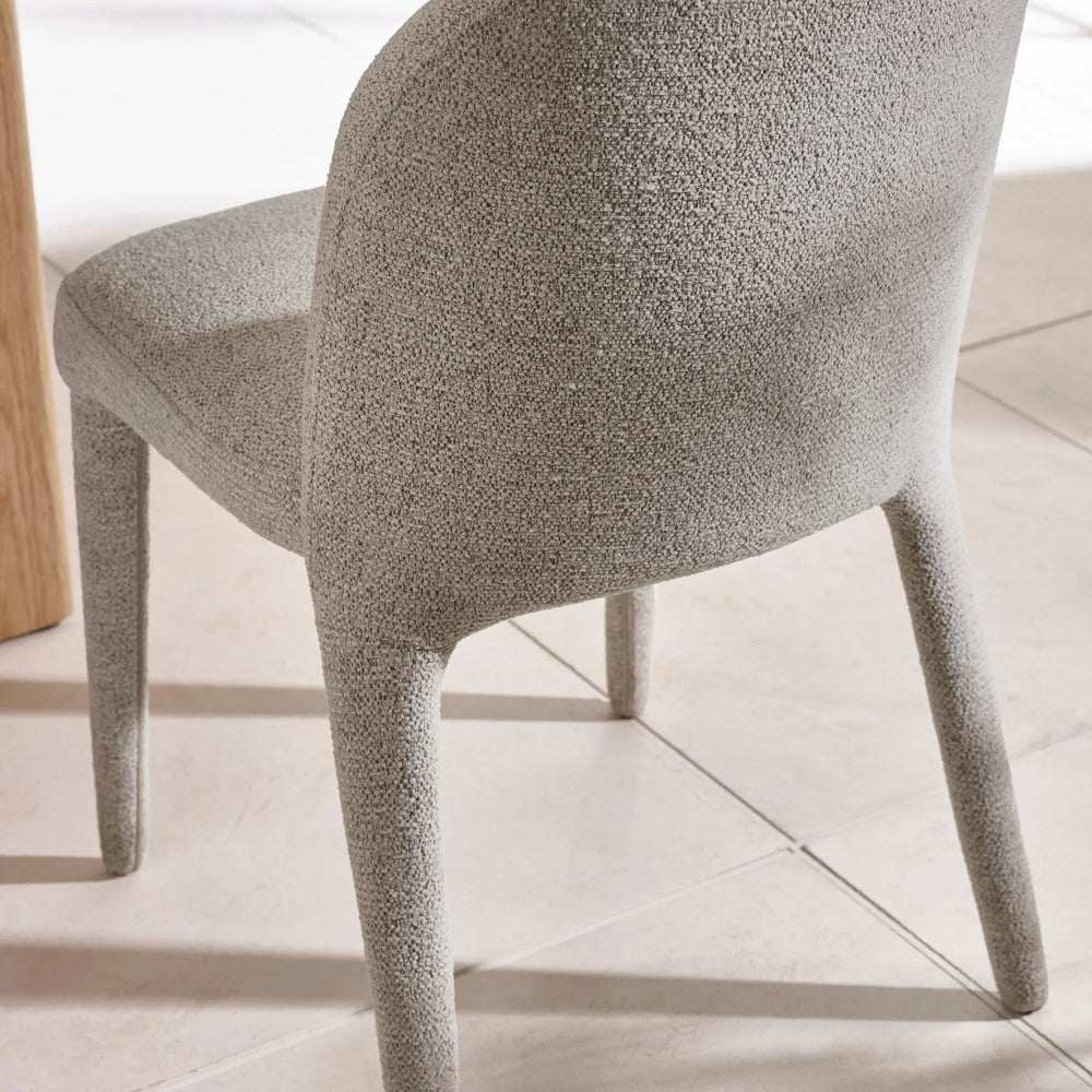 Light grey boucle dining chair with curved backrest on tiled floor
