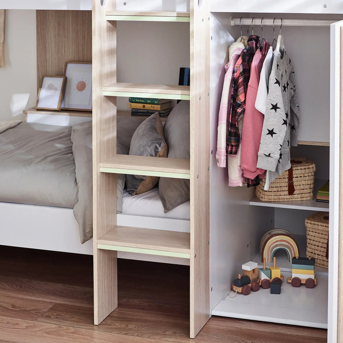 Pale wood bunk bed with open wardrobe, ladder shelves, and hanging children’s clothes