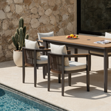 Light wood tabletop with dark grey frame chairs and beige cushions by a poolside.