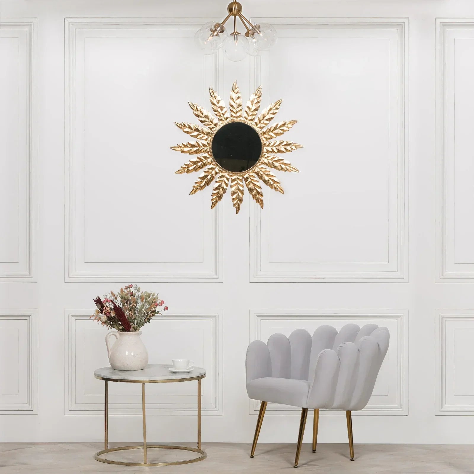 Gold sunburst wall mirror with black center above marble side table and grey accent chair