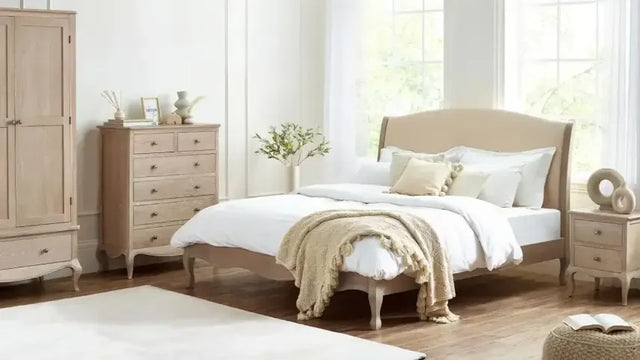 Beige upholstered bed with neutral bedding, wooden bedside table and dresser in bright bedroom