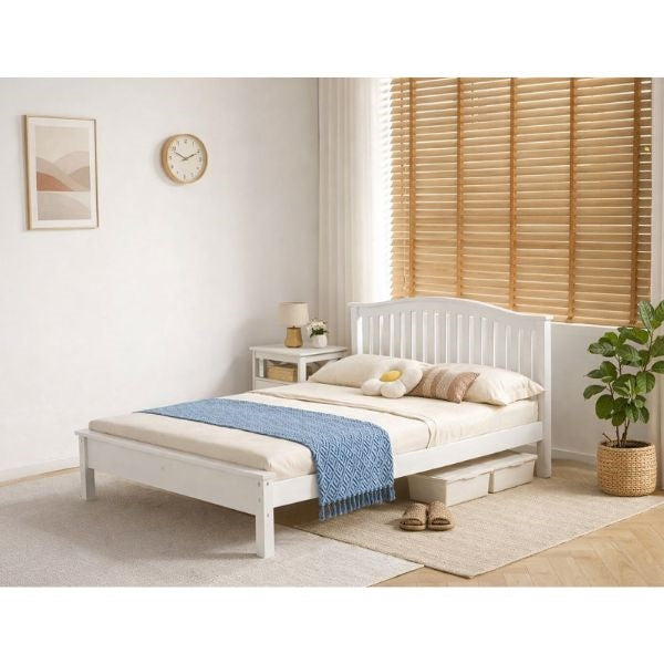 A single bed frame in a White finish, styled with cream bedding and a brown patterned throw blanket in a bright, modern bedroom setting with wooden blinds and a potted plant.