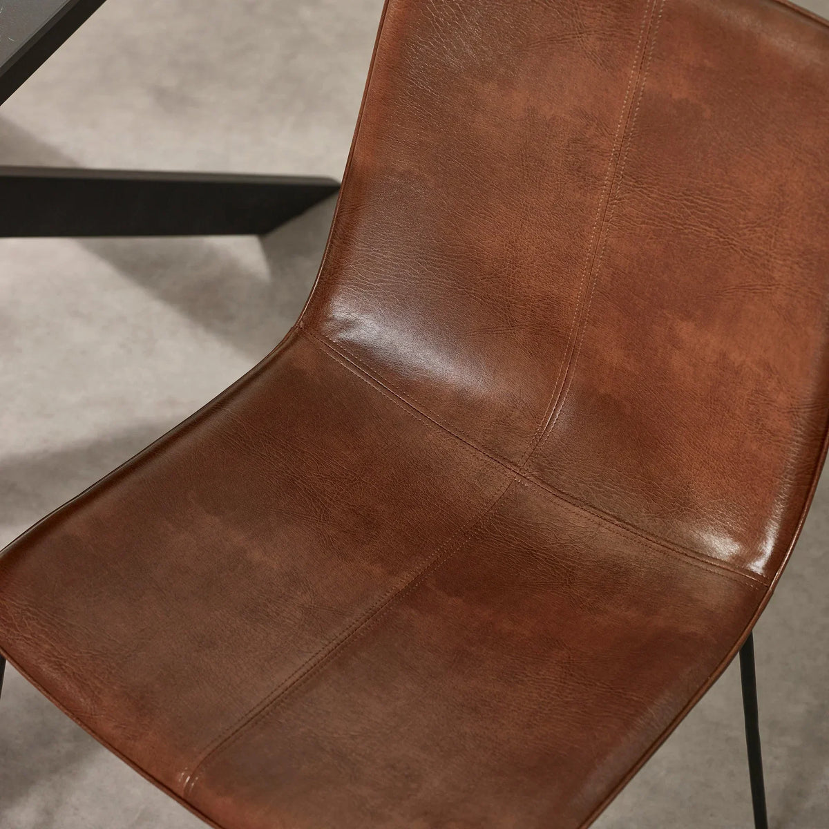 Brown faux leather dining chair with visible stitching and black metal legs