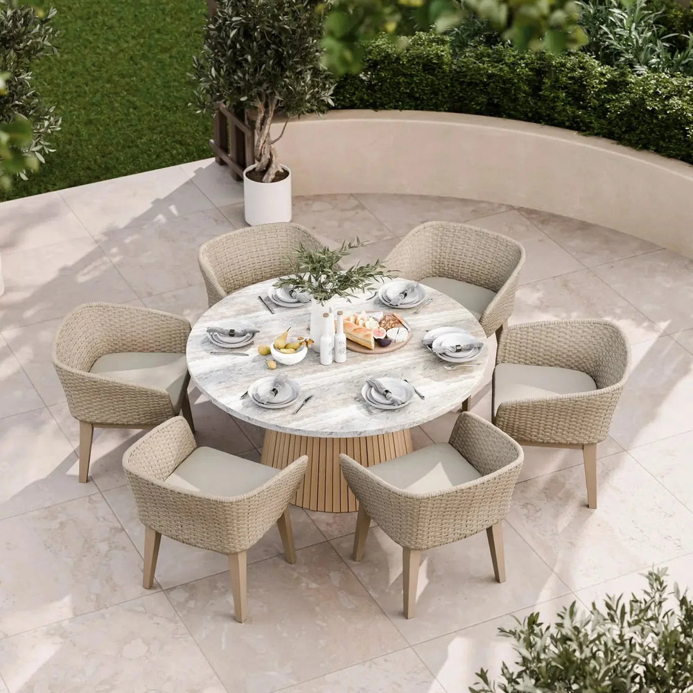 Round marble outdoor dining table with six wicker chairs on a patio, set for a meal