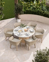 Round marble outdoor dining table with six wicker chairs on a patio, set for a meal