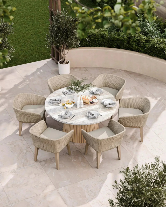 Round marble outdoor dining table with six wicker chairs on a patio, set for a meal