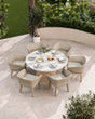 Round marble outdoor dining table with six wicker chairs on a patio, set for a meal