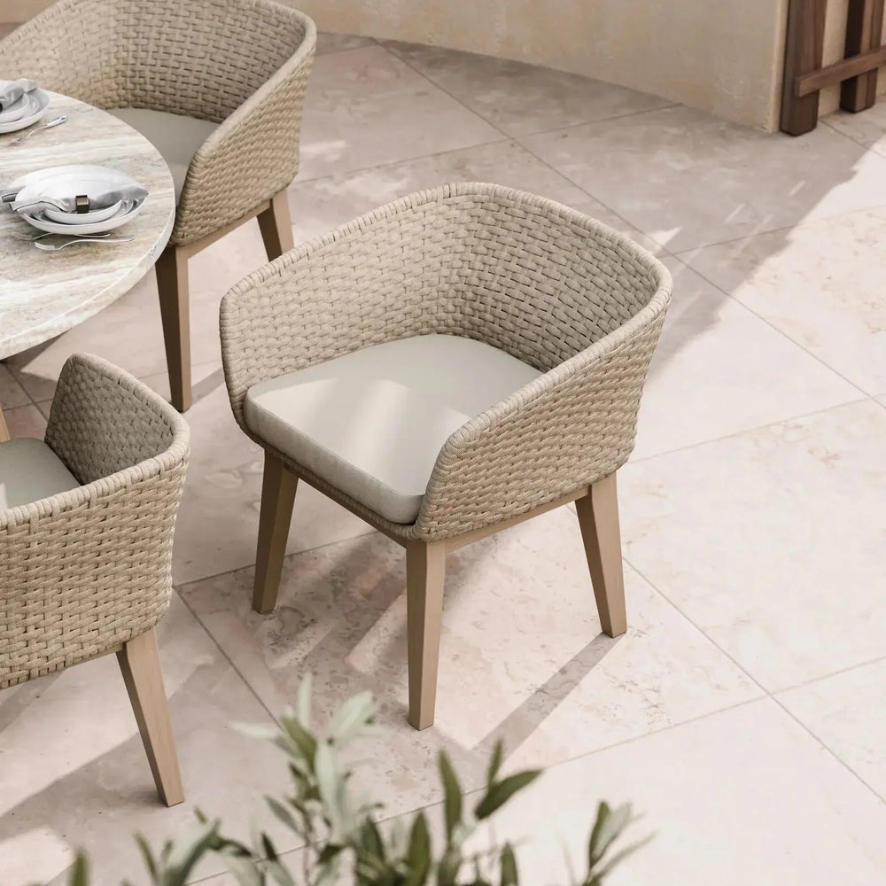 Beige rattan outdoor dining chair with cushioned seat beside round marble table on patio