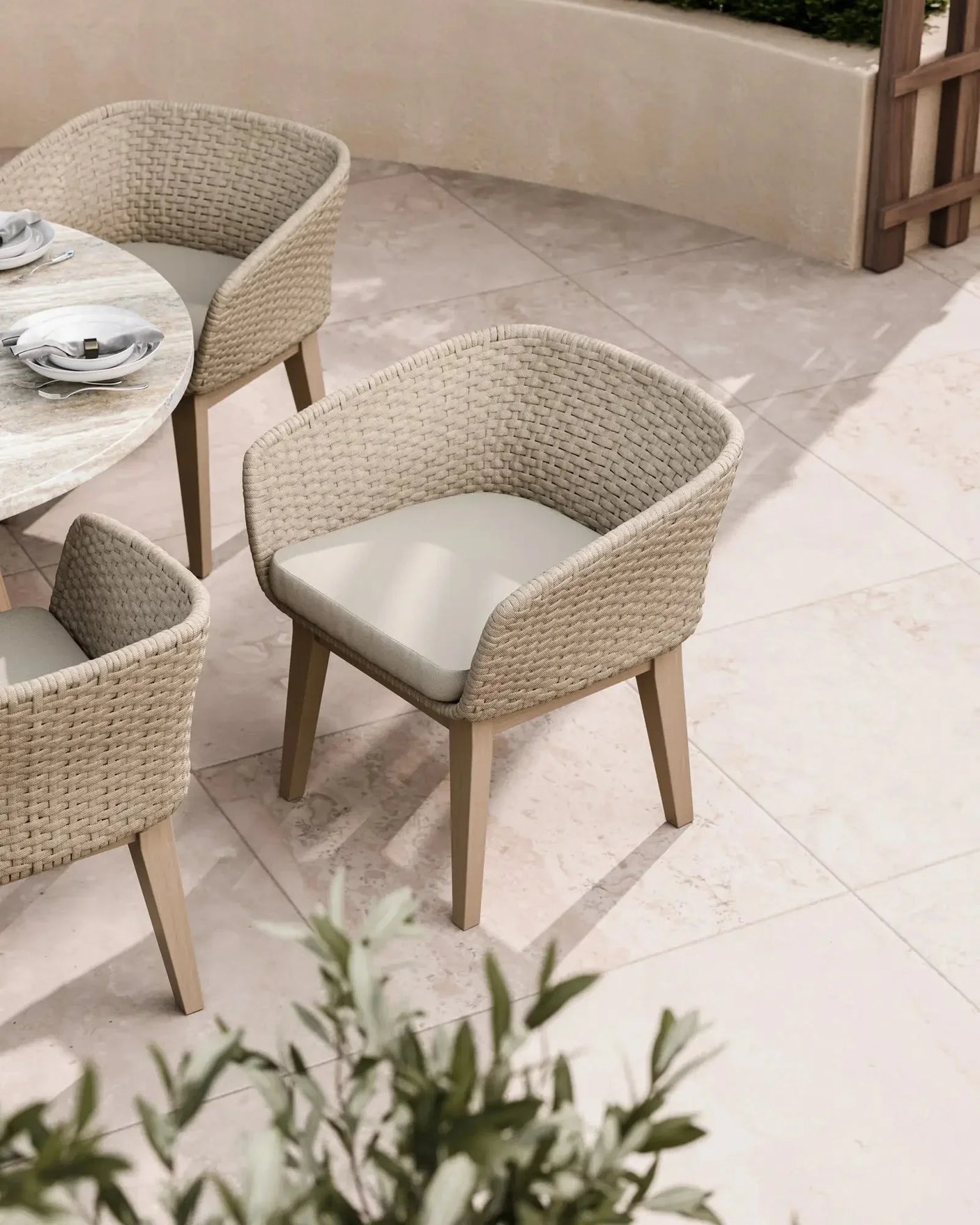 Beige rattan outdoor dining chair with cushioned seat beside round marble table on patio