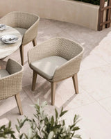 Beige rattan outdoor dining chair with cushioned seat beside round marble table on patio