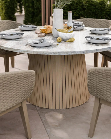 Round marble dining table with light wood base set for outdoor meal, woven chairs around