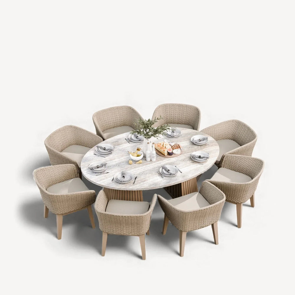 Oval dining table with light wood top and eight wicker armchairs, tableware set for eight