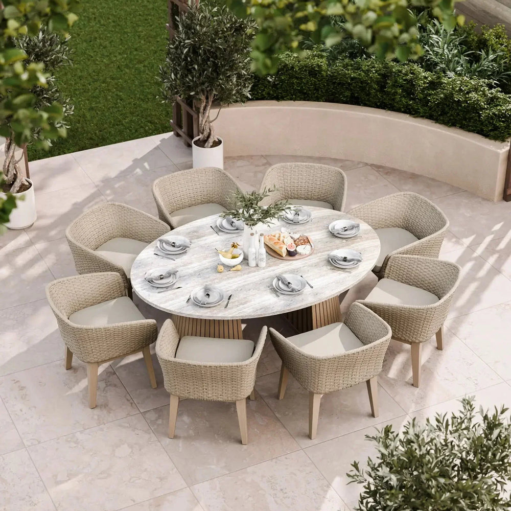 Oval garden dining table with eight wicker armchairs on stone patio set for outdoor meal