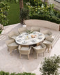 Oval garden dining table with eight wicker armchairs on stone patio set for outdoor meal