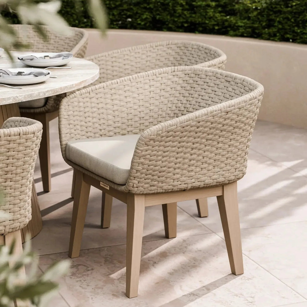 Rattan outdoor dining chair with light wood legs and cream cushion on tiled patio