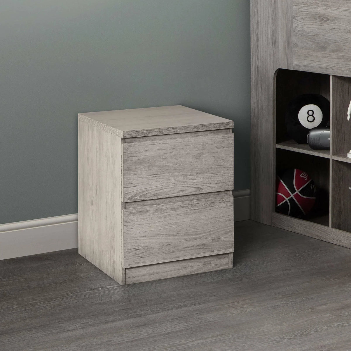 Grey oak bedside table with two drawers on wood floor beside shelving unit