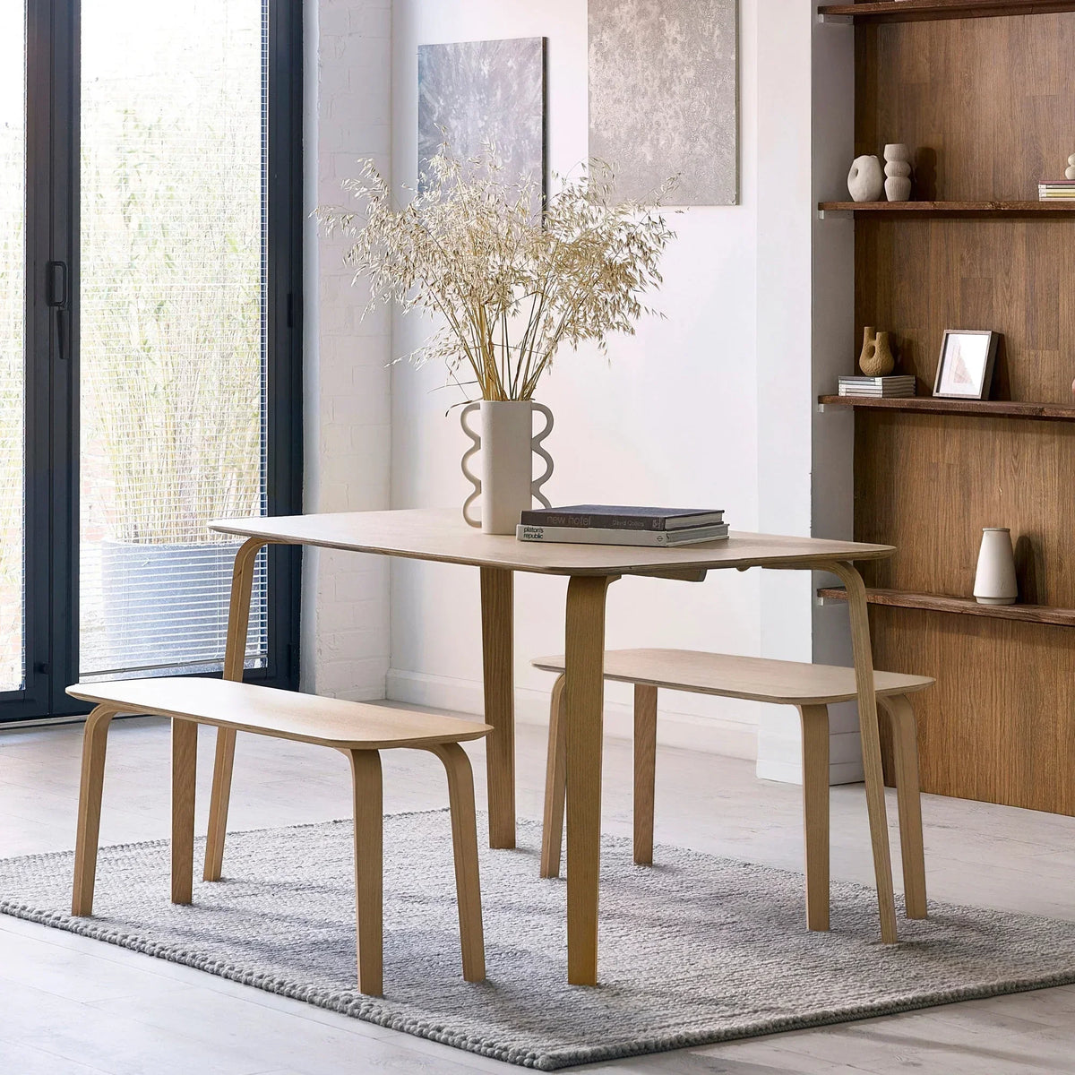Light wood dining table set with matching benches on a grey rug in modern dining room