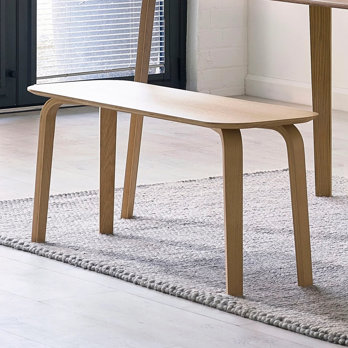 Light oak dining bench with curved legs on textured rug in modern room
