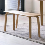 Light oak dining bench with curved legs on textured rug in modern room