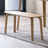 Light oak dining bench with curved legs on textured rug in modern room