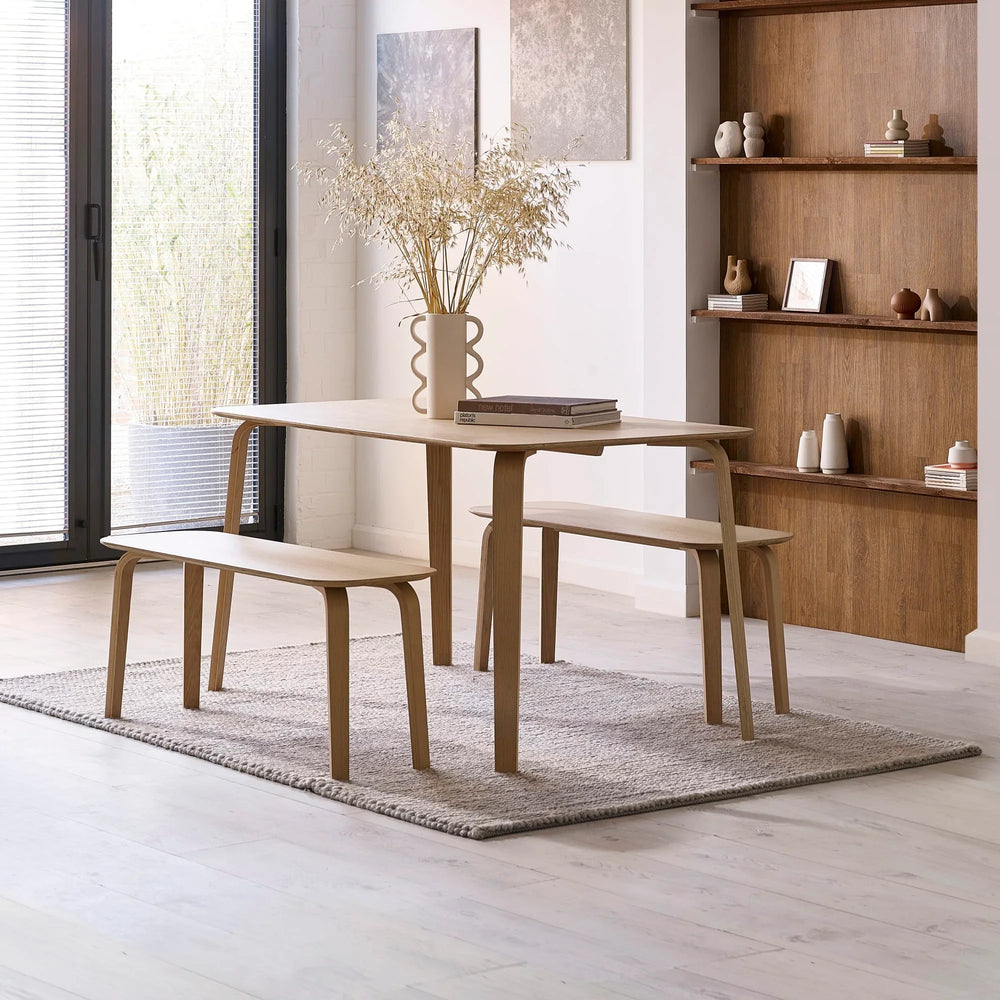 Oak dining table with matching benches on grey rug in modern living space with natural light