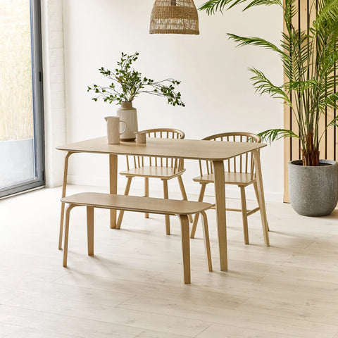 Light wood dining table set with bench and chairs in a modern room with plant decor
