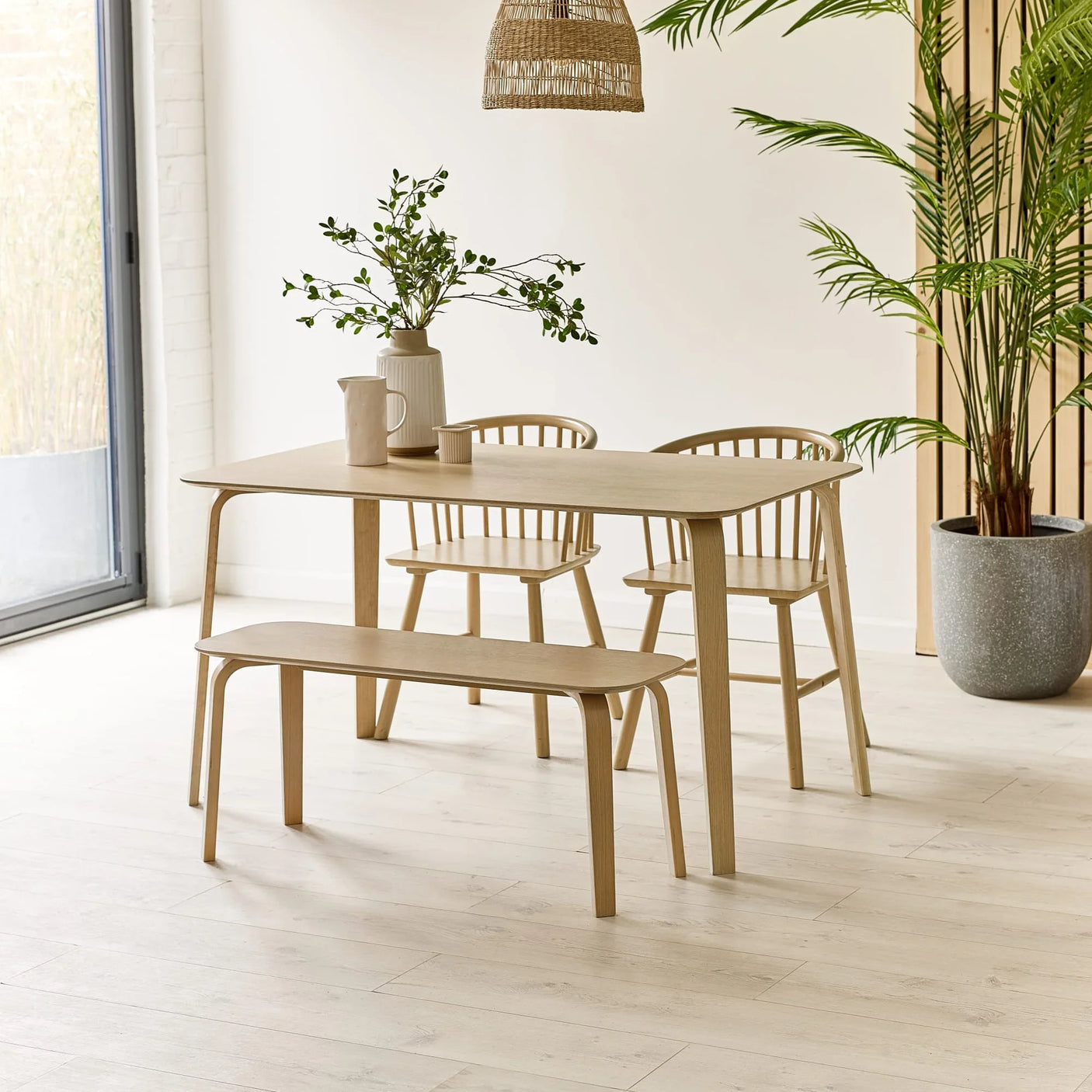 Light wood dining table set with bench and chairs in a modern room with plant decor