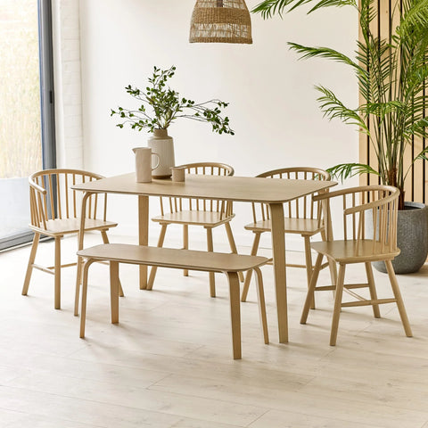 Light wood dining table set with four spindle back chairs and bench in bright modern room