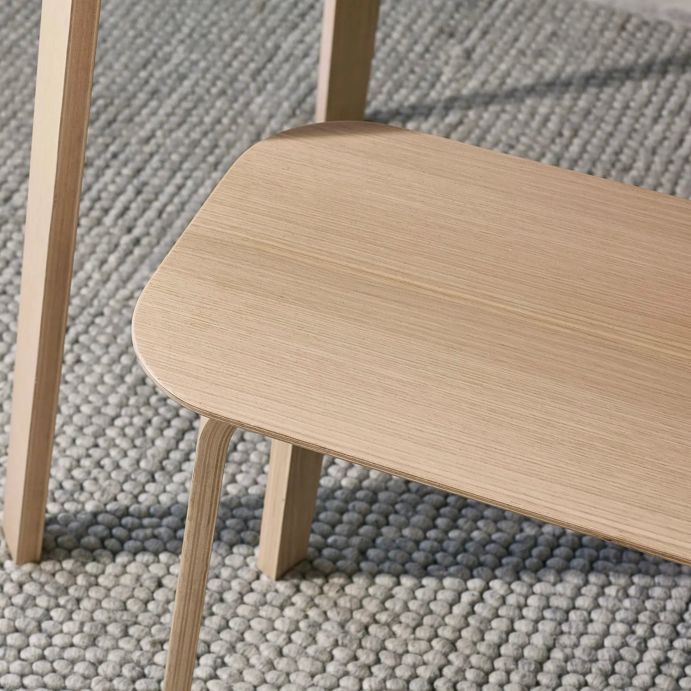 Light wood bench with smooth finish on textured grey rug, close angle view