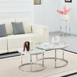 Two round nesting coffee tables with white marble-patterned tops and chrome metal bases, styled in a bright living room next to a cream sofa.