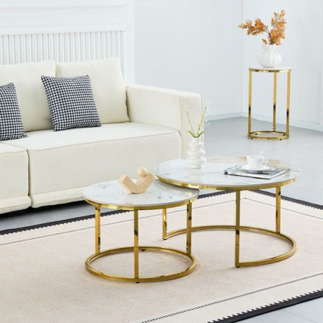 A modern nesting coffee table set with round white marble tops and gold-finished metal bases, styled in a bright living room next to a cream sofa.