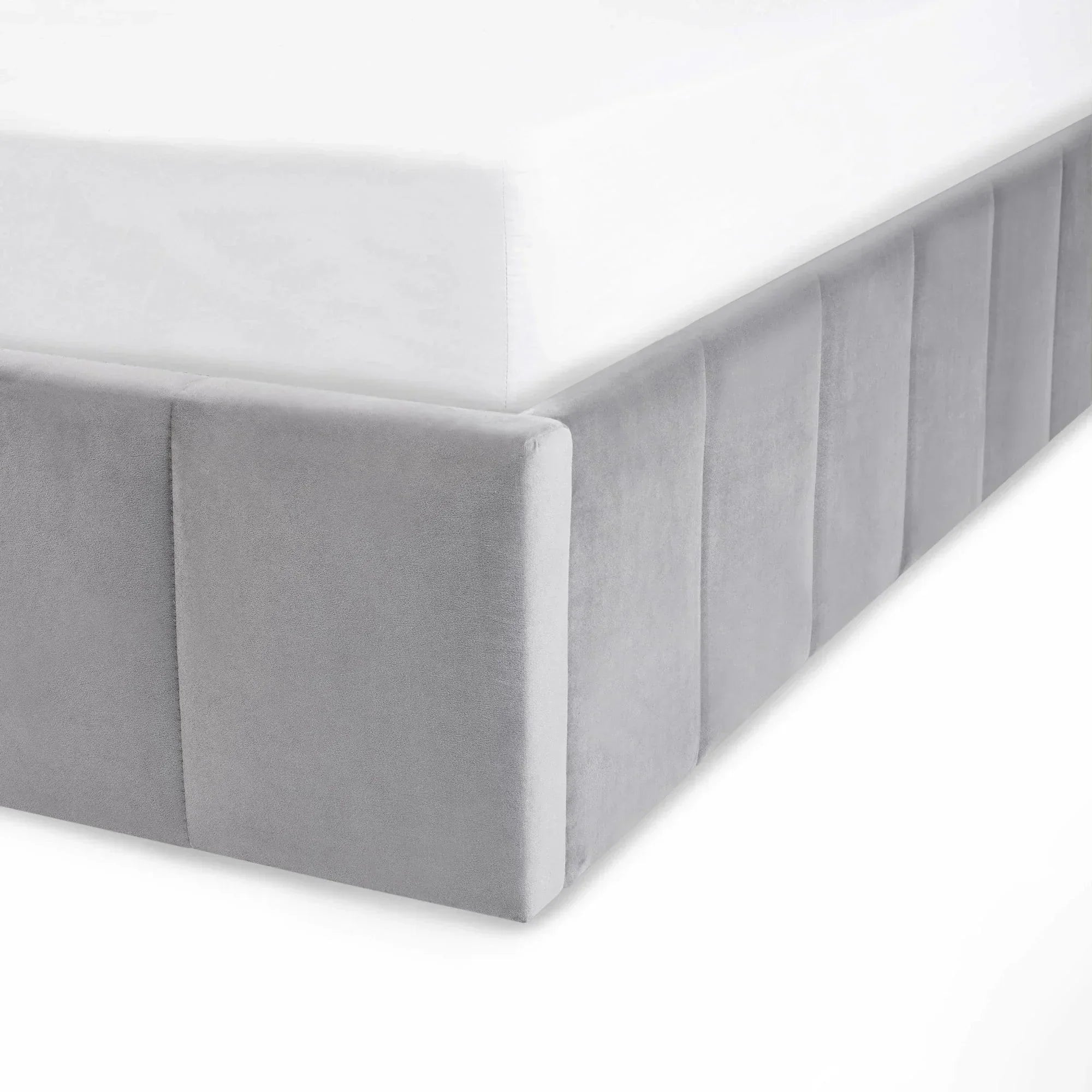 Light grey upholstered bed base corner with vertical panel detailing and white mattress