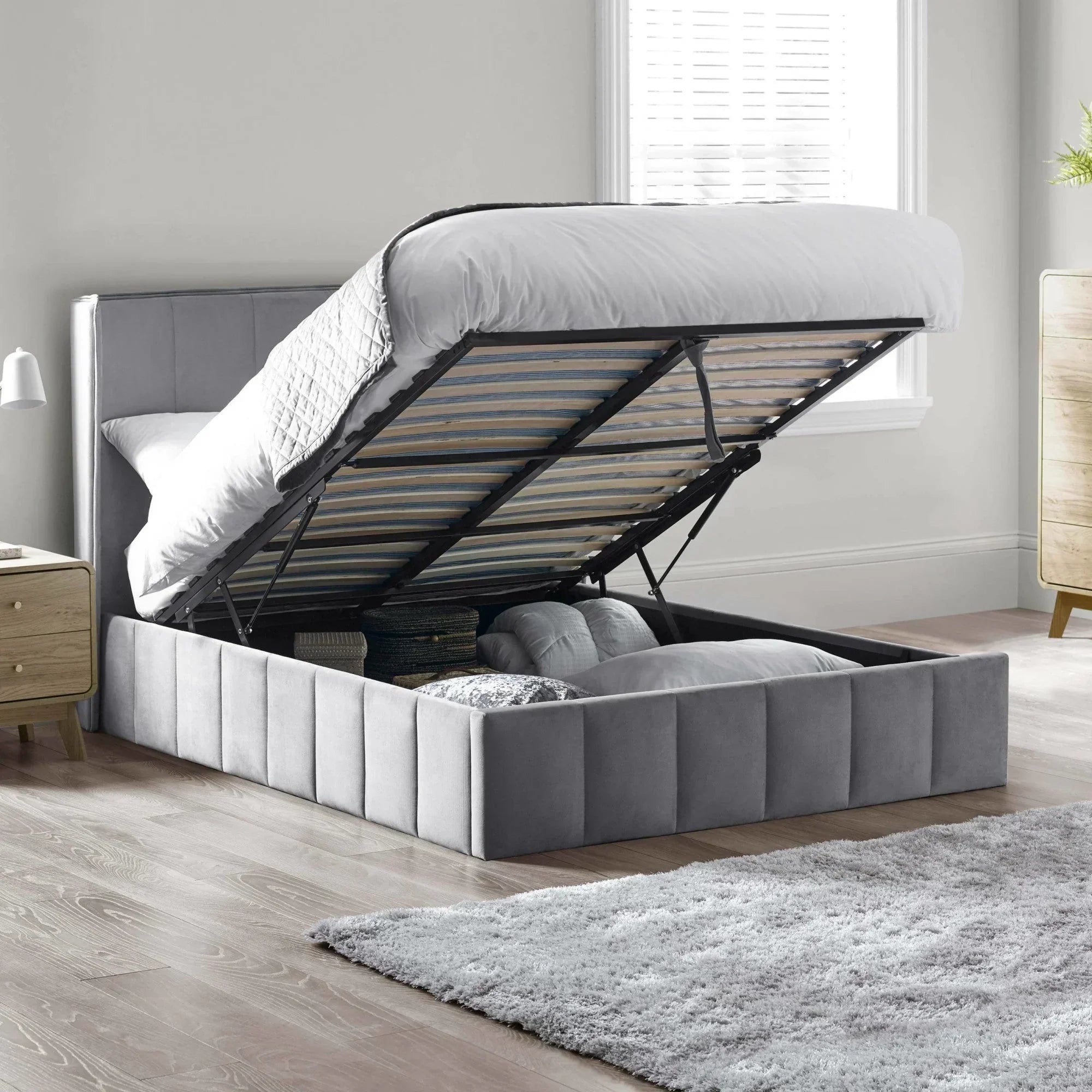 Grey ottoman storage bed with lifted mattress showing underbed storage compartments in bedroom