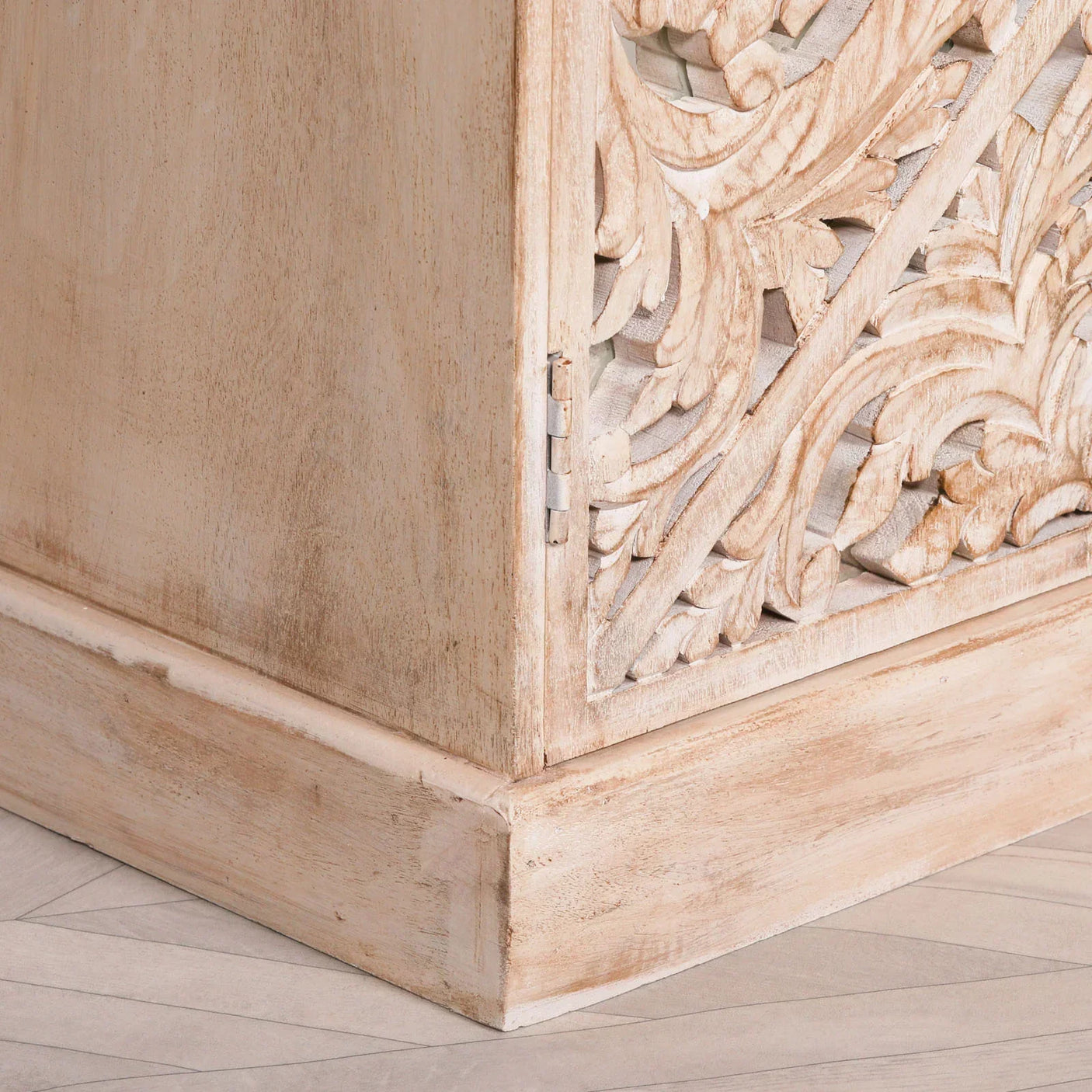 Carved wood cabinet corner with floral details and distressed light finish on tiled floor