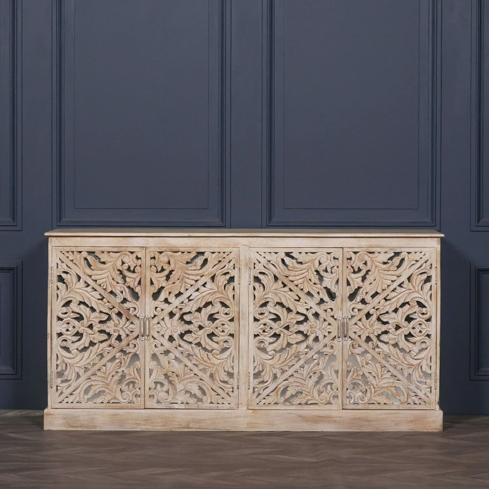 Carved wood sideboard with ornate floral patterns and light distressed finish against navy wall