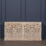 Carved wood sideboard with ornate floral patterns and light distressed finish against navy wall