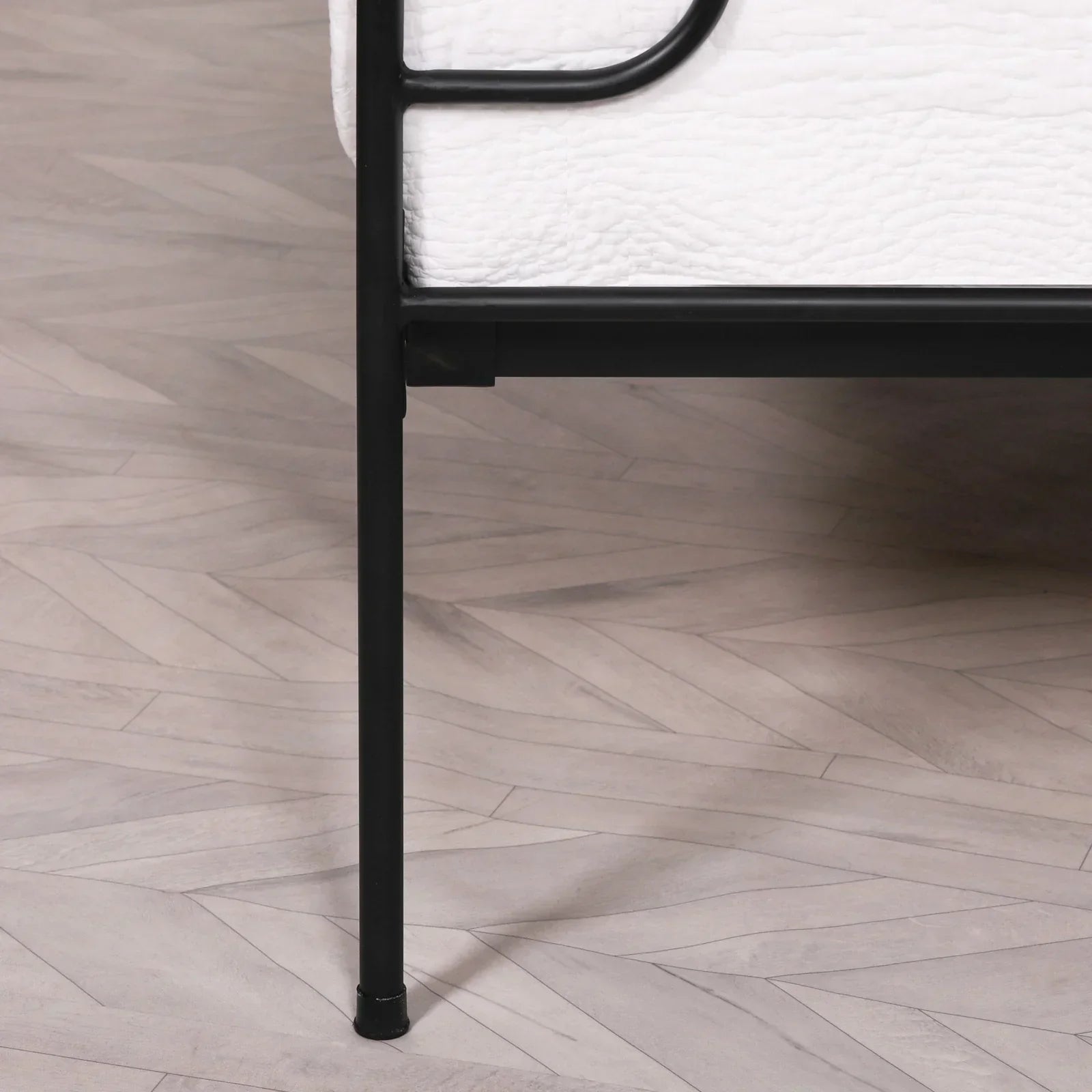 Black metal bed frame leg and white mattress on light herringbone wood floor