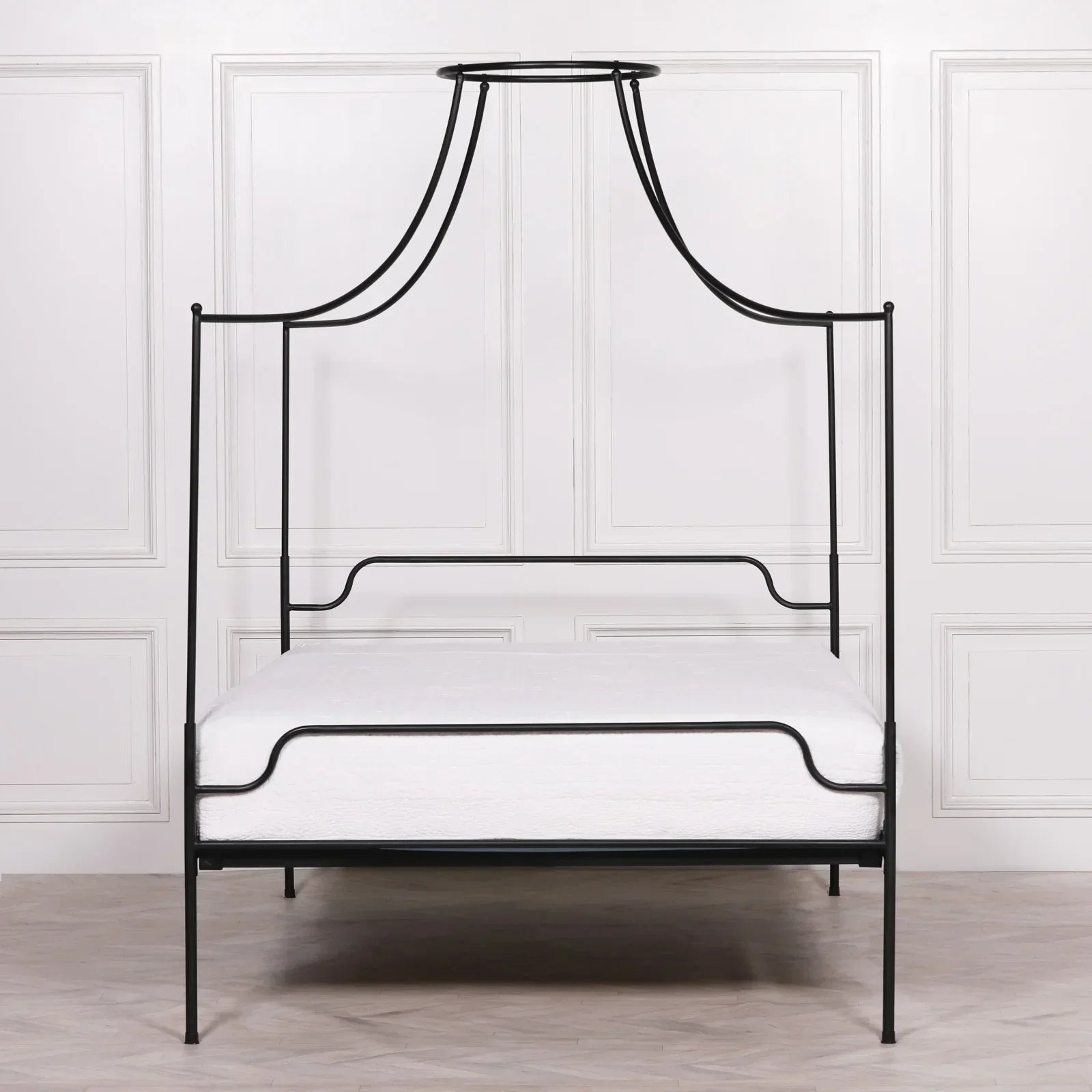 Black metal canopy bed frame with clean lines and white mattress in front of panelled wall