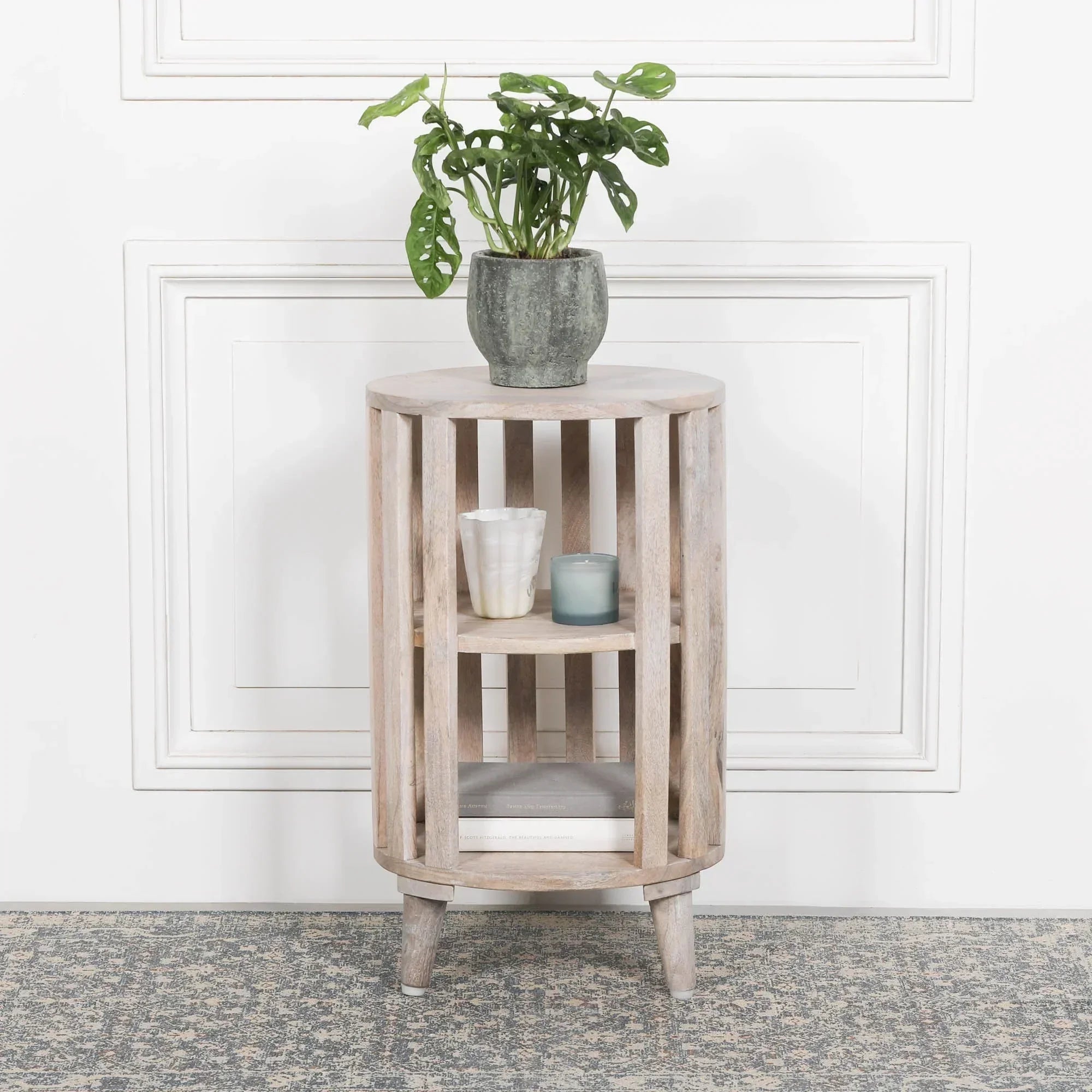 Round wooden side table with slatted design, indoor plant, candles, and books
