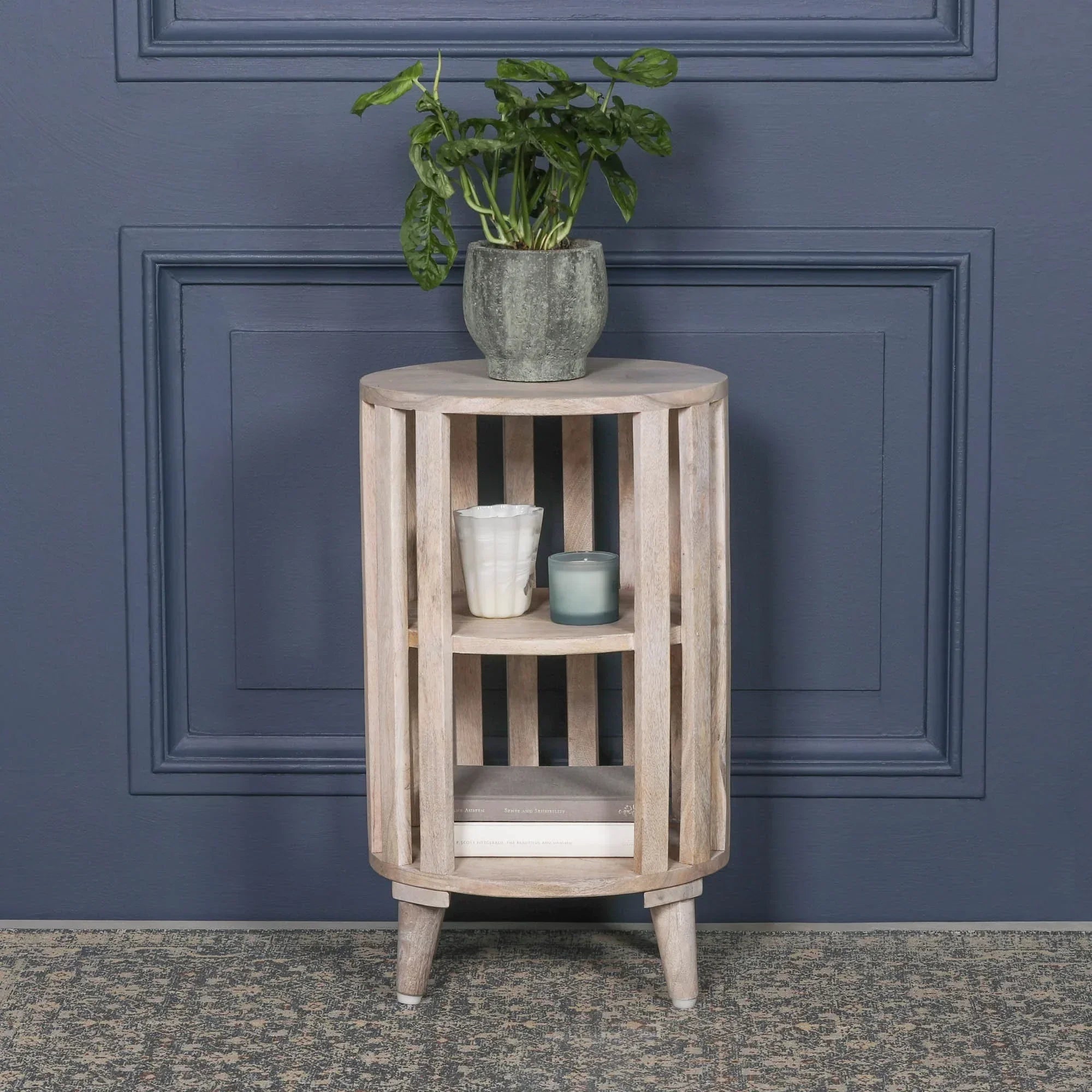 Wooden side table with slatted design, shelves, potted plant, candles, and books