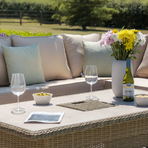 Rattan outdoor sofa set with beige cushions, glass table, wine, flowers and garden backdrop