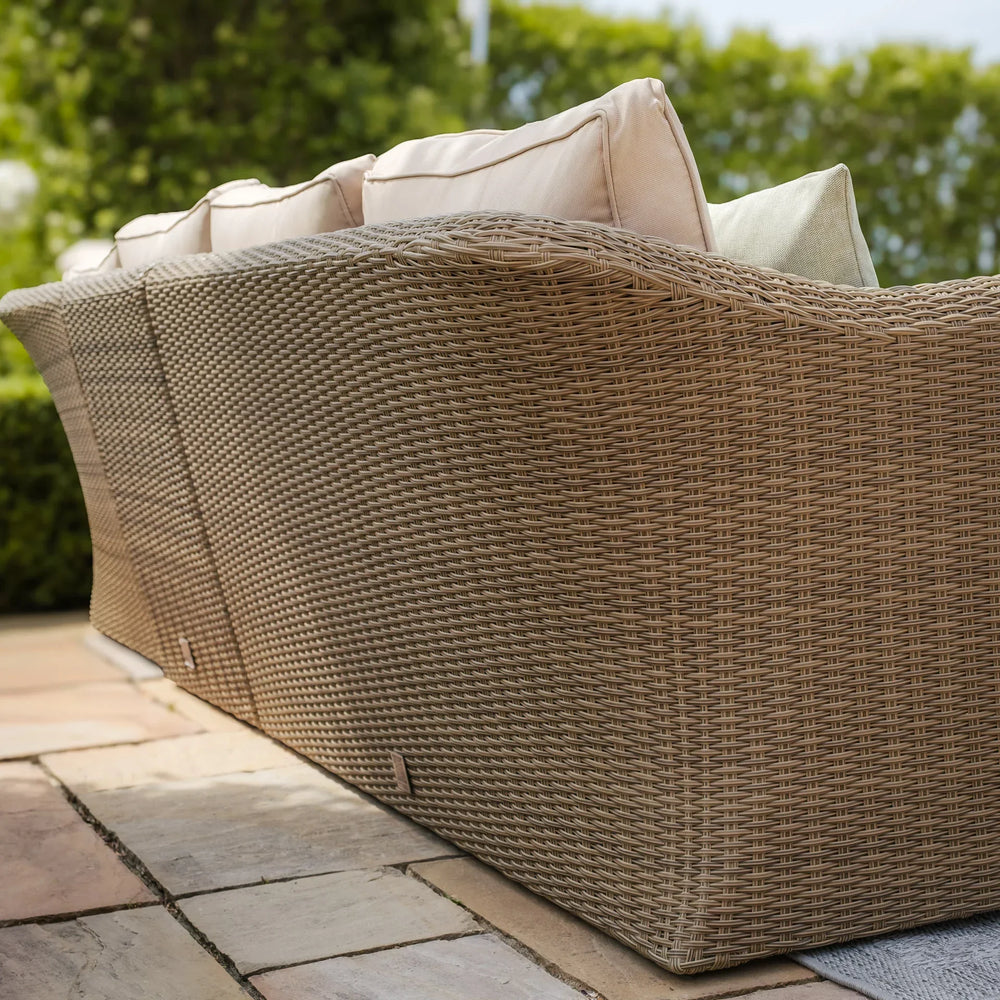 Curved rattan outdoor sofa with beige and green cushions on patio tiles