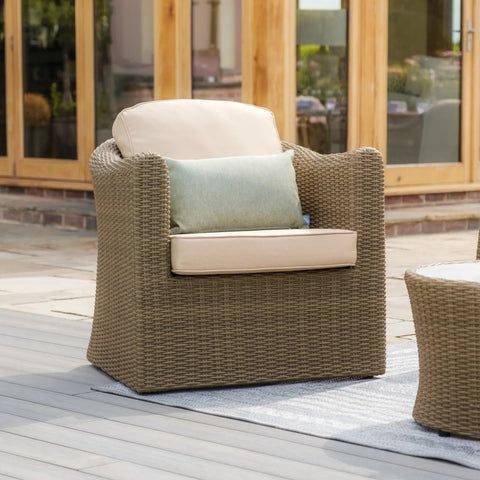 Rattan outdoor armchair with beige cushions and green accent pillow on patio decking